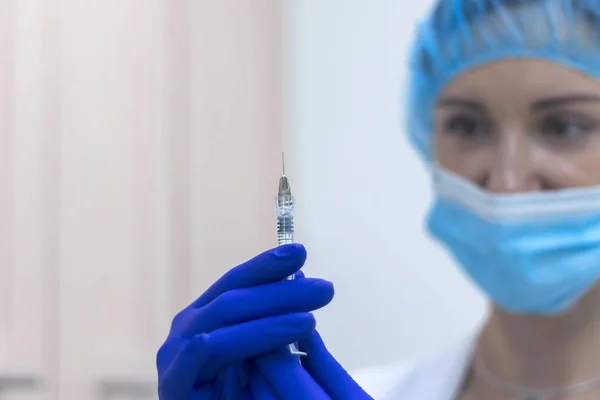 A woman doctor wearing gloves and a mask holding a syringe with a needle Concept of medicine and health care, The concept of vaccination against coronavirus.Selective focus, blurred background