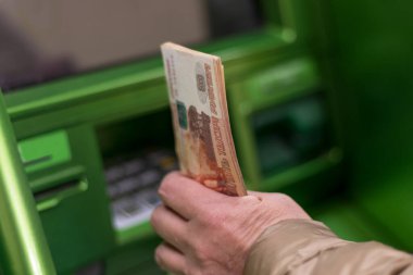 Saint Petersburg, Rusya, 04.30.2021, yaşlı bir kadın ATM 'nin yanında 5,000 ruble tutuyor. Nakit çekilmesi, kredi geri ödemesi