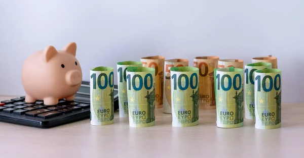 Hesap makinesinde bir domuz kumbarası ve 100 ve 50 avroluk banknotlar halinde her biri bir tomar banknota katlanmış kağıt para. Sermayeyi koruma ve artırma kavramı