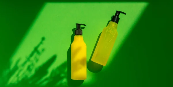 Plastic mock-up of yellow cosmetic bottles with shadow flowers on a green background. A creative, minimalistic snapshot of a cosmetic product. The concept of summer cosmetics. Flat lay