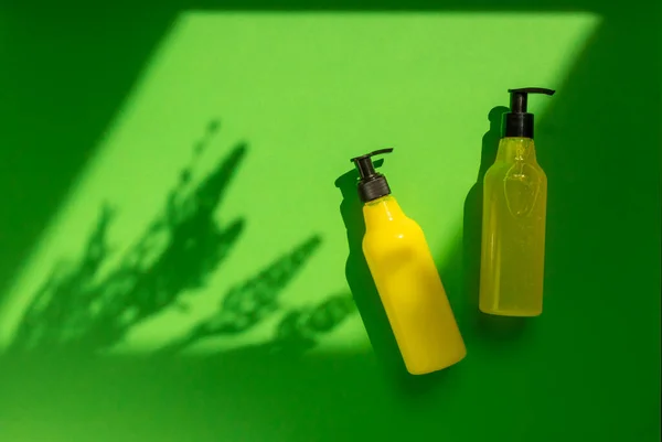 Plastic mock-up of yellow cosmetic bottles with shadow flowers on a green background. A creative, minimalistic snapshot of a cosmetic product. The concept of summer cosmetics. Flat lay