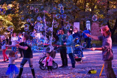 Krakow, Polonya - 12 Ekim 2019: Yeşil bir parkta çocuklarla çevrili bir su kabarcığı şişiren bir adam. Hafta sonu aile için boş zaman aktivitesi