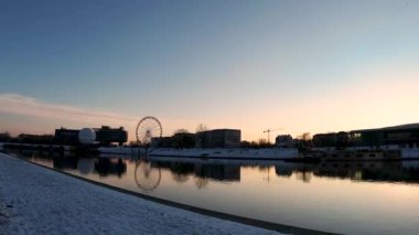 Krakow, Polonya - 31 Ocak 2021: Atlıkarıncaya karşı Vistula Nehri 'nin statik çekimi devam ediyor ve gün batımında şehir merkezinde yer alan binalar inşa ediliyor. Gün doğumuna karşı sakin nehir