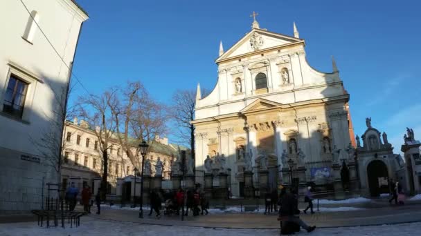 ポーランド クラクフ 2021年1月31日 グロドスカ旧市街の聖ピーター教会とポール教会に対して楽器を演奏する男の広い角度静的ショットと冬の間に散歩をする人々 — ストック動画