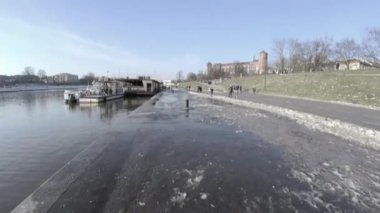 Krakow, Polonya: 01 Mart 2021: Polonya, Orta Avrupa 'daki ünlü wawel şatosuna karşı Vistula nehrinin yanında yürüyen ve boş zaman aktivitesi yapan insanları yukarı kaldır