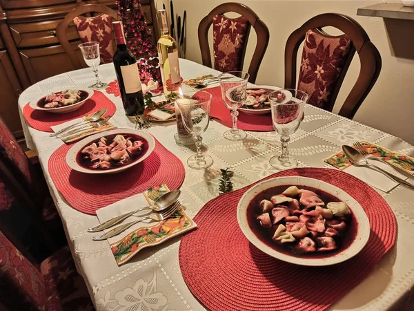 A dining table containing christmas eve lunch with food consists of Borscht beetroot soup with cabbage dumplings with wine bottles and glasses. Polish homemade dinner or lunch, Poland, Central Europe