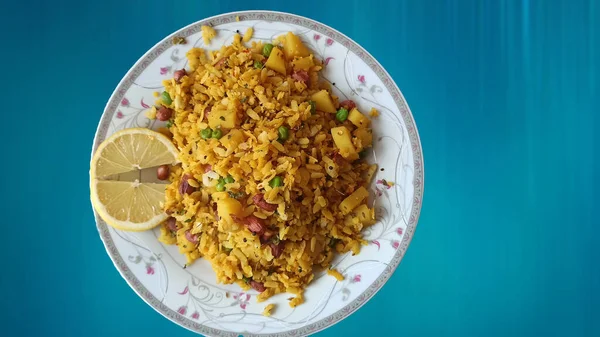 Tasty Indian cooked street food breakfast snack - Poha or Chivda made by flaked or flatten rice with slice of lemon on white plate against light blue plain background for copy paste text