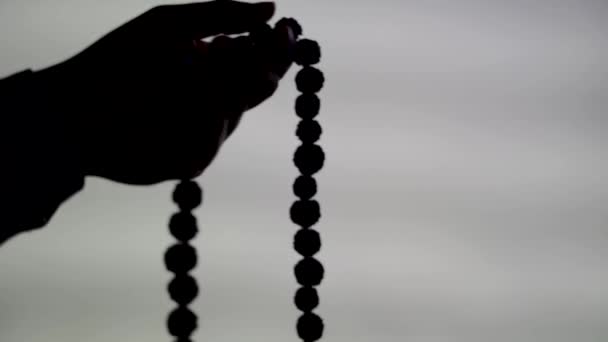 手に祈りのビーズのシルエットクリップ 男性の手 白い背景に神に祈るロザリオを保持し 宗教的な精神性 バラ色のビーズと瞑想を保持する男 宗教的概念 — ストック動画