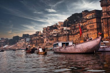 Varanasi, Hindistan - 01 Kasım 2016: Teknelerde turistlerin ve Uttar Pradesh 'te bulunan antik mimari ghat' ın bulunduğu kutsal Hindu ibadethanesinde dramatik bir gün batımı.