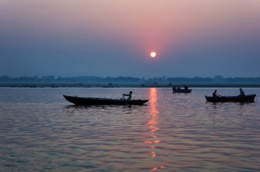 Varanasi, Hindistan - 01 Kasım 2016: Gündoğumunda veya günbatımında ünlü Munshi ghat yakınlarındaki Ganj nehrinde gezen ahşap tekne turistleri ve insanların geniş açılı görüntüsü.