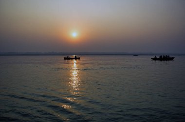 Varanasi, Hindistan: Şafak veya gün batımında ünlü Munshi ghat yakınlarındaki Ganj nehrine yakın ahşap tekne gezisi yapan insanlar ve turistlerin geniş açılı görüntüsü.