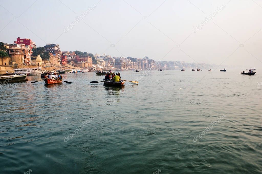 Varanasi, India - November 01, 2016: Tourist and pilgrim sightseeing on wooden boats in Ganges river against Ghat and Banaras cityscape during foggy weather.