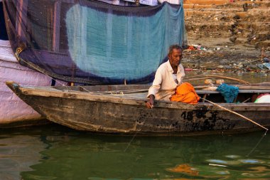 Varanasi, Hindistan - 01 Kasım 2016: Tahta bir teknede tek başına oturan yaşlı bir adam Uttar Pradesh eyaletinde yer alan Banaras şehrinde kurutulan bir kumaşla yaşamak için balık tutuyor.