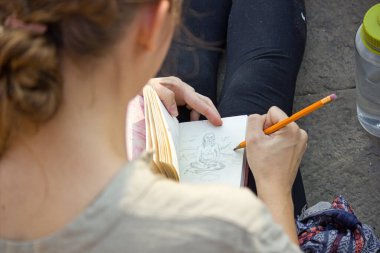 Over the shoulder shot of a girl drawing or sketching on a notebook diary using pencil during Indian travel visit in Varanasi, India. Uttar pradesh.