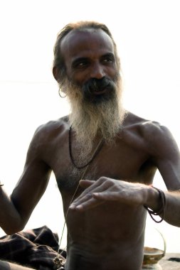 Varanasi, India - November 01, 2016: Portrait of a hindu bearded sadhu, pilgrim or Aghori baba talking to tourists while sitting against ganges river during daytime in banaras state of Uttar Pradesh