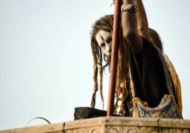 Varanasi, India - November 01, 2016: A hindu bearded sadhu, pilgrim or Aghori baba looking straight sitting with a stick against ganges river during day with dreadlocks