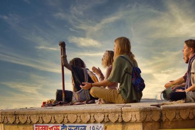 Varanasi, India - November 01, 2016: Bunch of tourists, sadhu baba and pilgrims in sitting posture meditating together on a pile of rock during morning facing ganges river and sunrise. Uttar pradesh