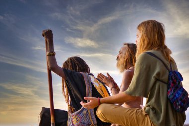 Varanasi, India - November 01, 2016: Bunch of tourists, sadhu baba and pilgrims in sitting posture meditating together on a pile of rock during morning facing ganges river and sunrise. Uttar pradesh