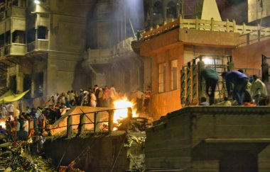 Varanasi, Hindistan - 01 Kasım 2016: Banaras 'ın kutsal Manikarnika Ganj nehri ghat manzarası ve antik şehir mimarisi ve geceleri yakılmak üzere yakılan ahşap kütükler. Uzun pozlu çekim