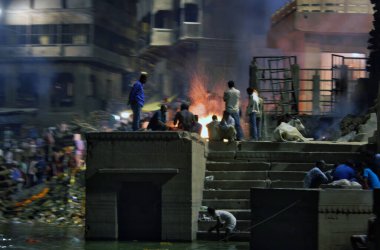 Varanasi, Hindistan - 01 Kasım 2016: Banaras 'ın kutsal Manikarnika Ganj nehri ghat manzarası ve antik şehir mimarisi ve geceleri yakılmak üzere yakılan ahşap kütükler. Uzun pozlu çekim