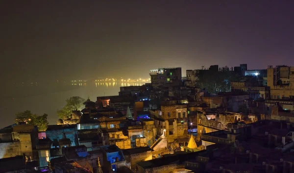 Historical indian city Varanasi, view over rooftop of the poor brick buildings, India. Aerial cityscape of Banaras ancient old architecture illuminated during night with mist in the background