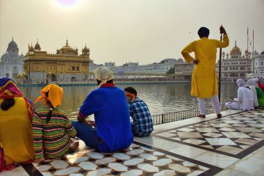 Amritsar, Hindistan - 06 Kasım 2016: Gölün kenarında kimliği belirsiz bir ziyaretçi ve hacı ve Sih 'in ünlü Altın Tapınağı' na bakan bir erkek güvenlik görevlisi Dastar 'ı takıyor
