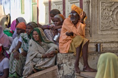 Pushkar, Hindistan - 10 Kasım 2016: Bir grup yoksul insan türbanlı bir erkekten ve Rajasthan eyaletinde gölgede oturmuş otobüs bekleyen sarili kadınlardan oluşuyor