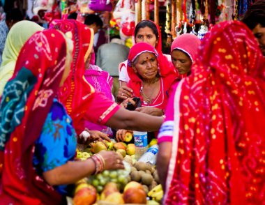 Pushkar, Hindistan - 10 Kasım 2016: Rajasthan eyaletinde başlarını örterken çok az sayıda renkli sari giymiş Hintli kadın grup halinde meyve satın alıyor