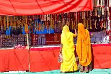 Geleneksel Hindu kökenli kimliği belirsiz iki kadın Hindistan 'ın Rajasthan eyaletindeki Pushkar fuarının ticari caddesinde sari ya da mücevher alışverişi yapıyorlar. Renkli Hint kültürü konsepti