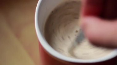 Kahve fincanında şeker karıştıran bir el. Günaydın konsepti. Kırmızı bardakta kapuçino..