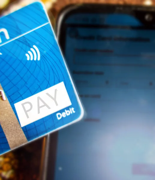 Close up of a debit or credit card making online payment through mobile phone to pay bills.