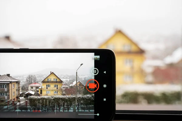 Close-up of screen of phone taking video or picture. Action. Phone screen shooting video of houses in winter during snow fall weather. compact mobile phone photography or videography concept.