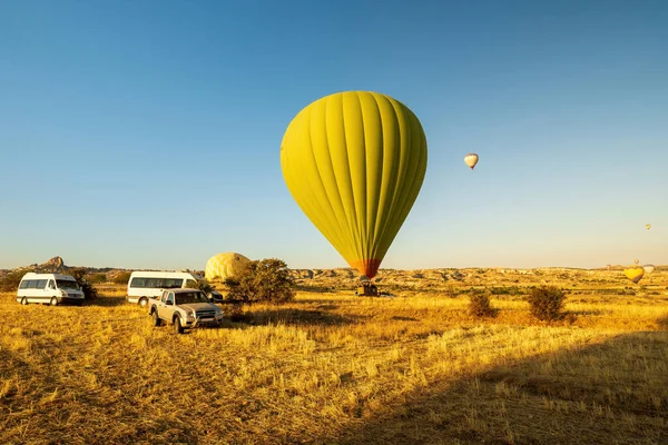 Two hot-air balloons taking off or landing in a field. One is on the ground. The other is airborne with crew member in vehicle ready to support in Cappadocia, Turkey