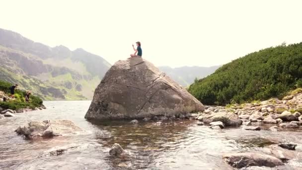 ザコパネ ポーランド 2021年8月15日 高タトラのPieciu Stawow Polskieの谷に位置するRoztokaストリームや川として流れる水の池の岩の上に座って写真を撮る男 — ストック動画