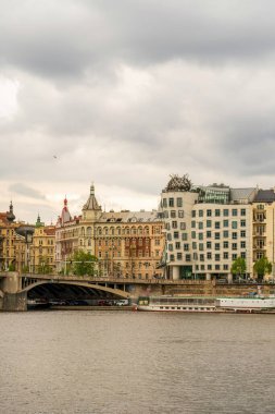 Prag nehir kenarı mimarisi Dansçı Evi, Vltava Nehri, tarihi köprüler, bulutlu gökyüzü altında renkli binalar, deniz manzarası