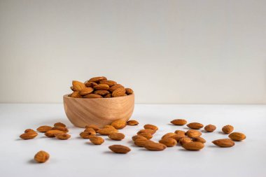 Kahverengi ahşap bir kasede beyaz masa arkasında badem..