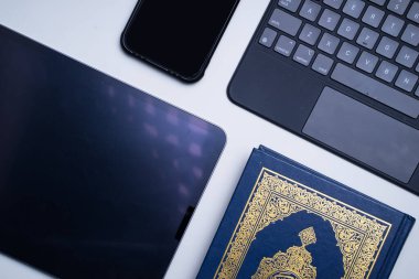 Teknoloji cihazlarının ve uygulamaların Kuran 'ı dijitalleştirmeye veya e-Kuran' a uygulanması. Çevrimiçi öğrenme ya da uygulamaları kullanarak Kur 'an resitali. Kitabın üzerindeki Arapça kelimeler kutsal Kur 'an anlamına gelir.