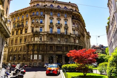 Milano sokak panoramasında güneşli bir günde Milan tramvayları, yayalar ve arabalar.