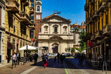 Milano sokak panoramasında güneşli bir günde Milan tramvayları, yayalar ve arabalar.