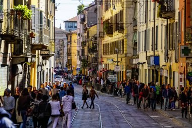 Milano sokak panoramasında güneşli bir günde Milan tramvayları, yayalar ve arabalar.
