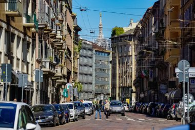 Milano sokak panoramasında güneşli bir günde Milan tramvayları, yayalar ve arabalar.
