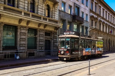 Milano sokak panoramasında güneşli bir günde Milan tramvayları, yayalar ve arabalar.
