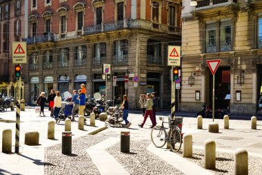 Milano sokak panoramasında güneşli bir günde Milan tramvayları, yayalar ve arabalar.