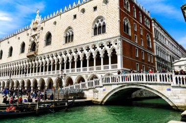 Venedik 'te yüzen Gondolalar ve turistler Riva degli Schiavoni rıhtımında arka planda The Doge' s Palace ile güzel bir günün tadını çıkarıyorlar.. 