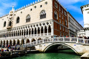 Venedik 'te yüzen Gondolalar ve turistler Riva degli Schiavoni rıhtımında arka planda The Doge' s Palace ile güzel bir günün tadını çıkarıyorlar.. 