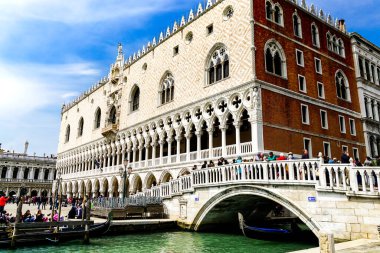 Venedik 'te yüzen Gondolalar ve turistler Riva degli Schiavoni rıhtımında arka planda The Doge' s Palace ile güzel bir günün tadını çıkarıyorlar.. 