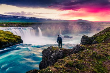 Godafoss Şelalesi 'nde fotoğrafçıyla yaz sabahı sahnesi. İzlanda, Avrupa 'daki Skjalfandafljot nehrinde renkli bir gün doğumu. İşlenmiş fotoğraf sonrası sanatsal stil.