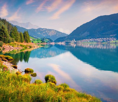 Resia (Reschensee) gölünde renkli yaz gündoğumu. Sabah sisinde Resia köyü, Bolzano ili - Güney Tyro, İtalya, Avrupa. İşlenmiş fotoğraf sonrası sanatsal stil.