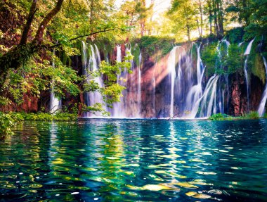 Son güneş ışığı Plitvice Ulusal Parkı 'ndaki saf su şelalesini aydınlatıyor. Mavi göllü yeşil ormanın renkli bahar manzarası. Hırvatistan ve Avrupa 'nın kırsal manzarası harika. Doğa konseptinin güzelliği.