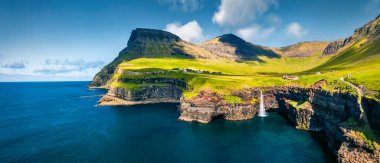 Uçan İHA 'nın görüntüsü. Mulafossur Şelalesi 'nin şaşırtıcı sabah sahnesi. Gasadalur köyünün panoramik yaz manzarası, Vagar, Faroe Adaları, Danimarka Krallığı, Avrupa. Seyahat konsepti arka planı